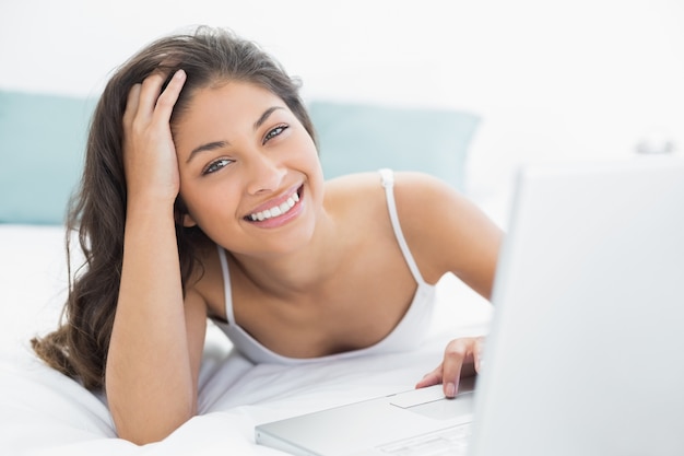 Smiling casual woman using laptop in bed