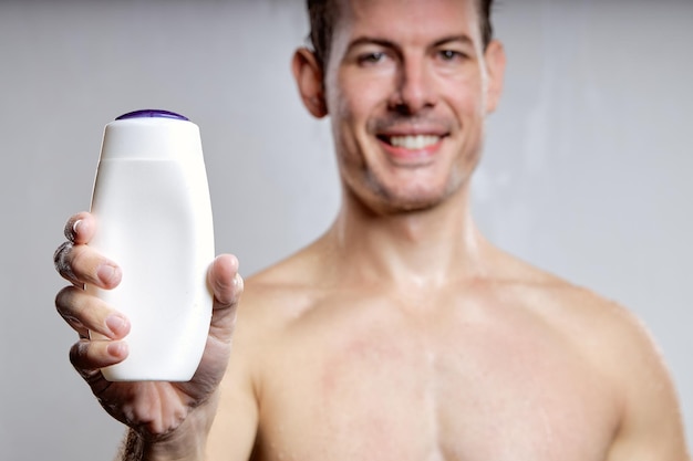 Smiling caucasian guy showing bottle of gel or shampoo for advertisement focus on bottle