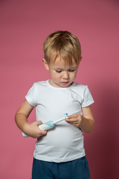 Smiling caucasian little boy holds electric sonic toothbrush on pink background.