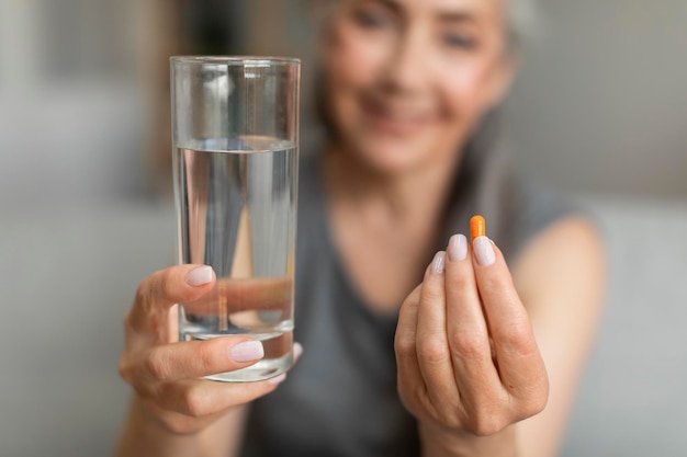 Smiling caucasian retired woman show glass of water and pill of vitamins painkillers or