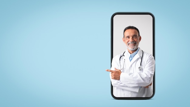 Smiling caucasian senior doctor therapist in white coat point finger on free space on big phone