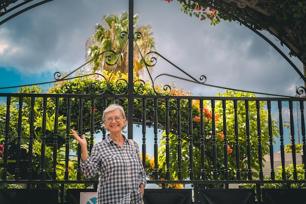 Smiling caucasian senior woman walking outdoors in a flowered garden looking at camera Relaxed retirement lifestyle