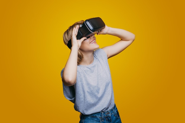 Smiling caucasian woman wearing virtual headset using vr glasses yellow wall background future techn...