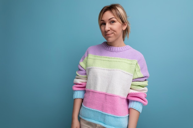 Smiling charming blond young woman in a striped sweater on a blue background with copy space