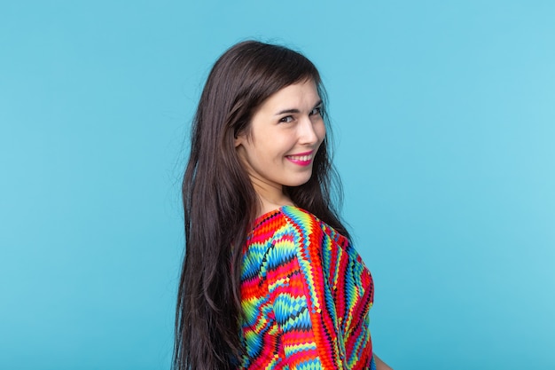 Smiling charming young brunette woman standing against a blue wall with copy space.