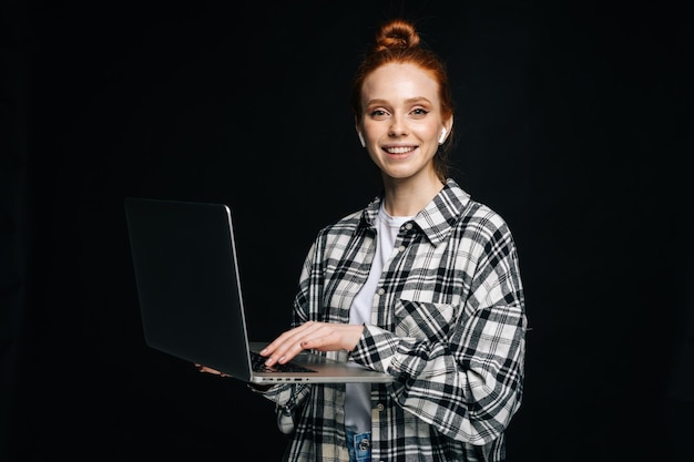 Smiling charming young business woman or student holding laptop computer and looking at camera