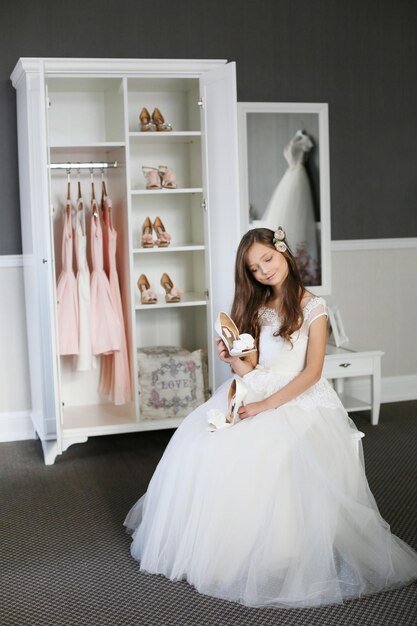 Smiling cheerful little girl in a beautiful white ball gown and sneakers sitting on the stairs to the outdoors