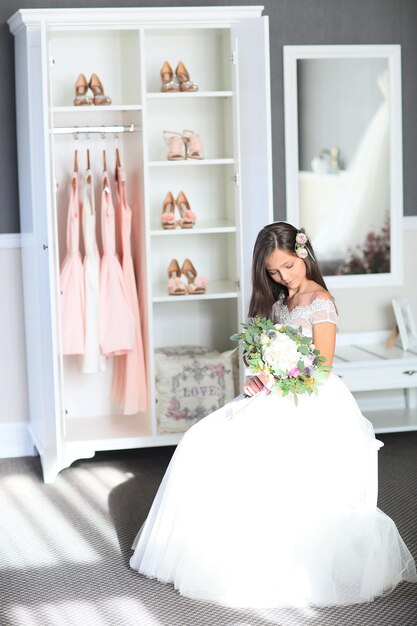 Smiling cheerful little girl in a beautiful white ball gown and sneakers sitting on the stairs to the outdoors