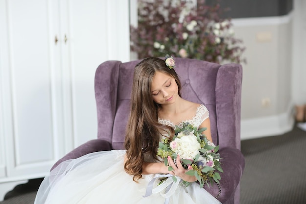 Smiling cheerful little girl in a beautiful white ball gown and sneakers sitting on the stairs to the outdoors