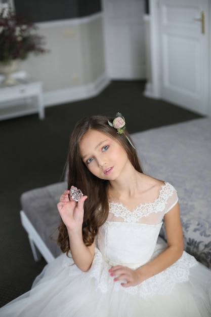 Smiling cheerful little girl in a beautiful white ball gown and sneakers sitting on the stairs to the outdoors