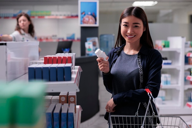 Smiling cheerful pharmacy customer holding basket looking at shelves with health care products buying supplements. Client choosing vitamins for immune system in pharmaceutics shop