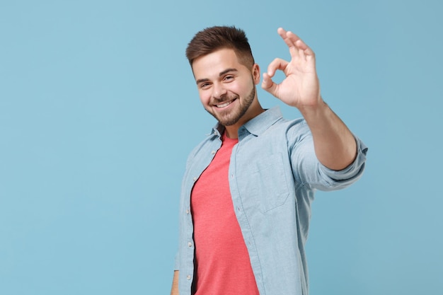 Smiling cheerful young bearded guy 20s in casual shirt posing isolated on pastel blue background studio portrait. People sincere emotions lifestyle concept. Mock up copy space. Showing OK gesture.