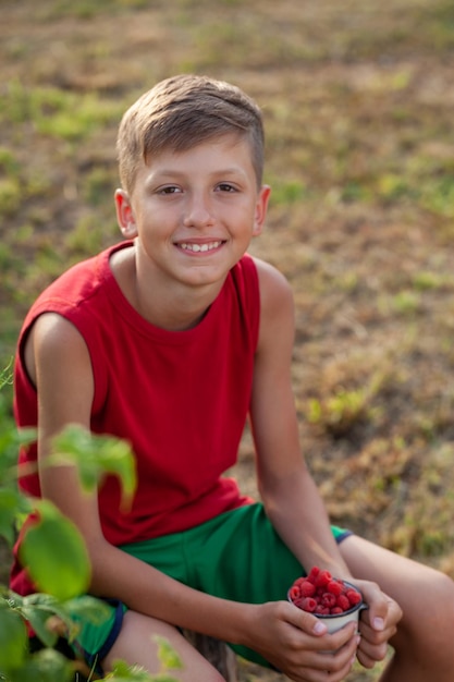 Smiling child holding full jar of fresh raspberries ready to eat on a summer day.