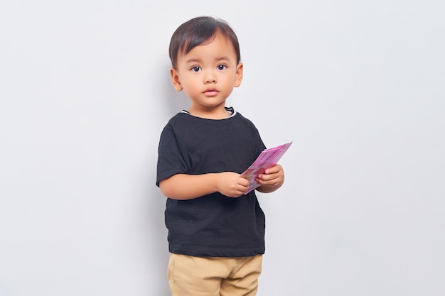 Smiling child kid boy 2 years wearing black tshirt holding Indonesian rupiah banknotes isolated on white background