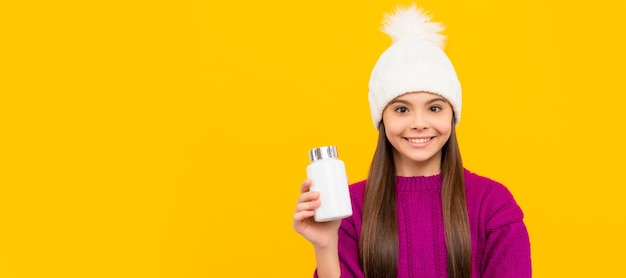 Smiling child in winter hat with pill jar food supplement teen girl with natural pill products