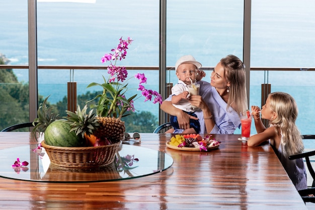 Smiling children having fresh juice from tropical fruits in kitchen with their mother