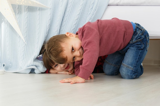 Photo smiling children playing indoor boy and girl playing hiding under bed happy children concept