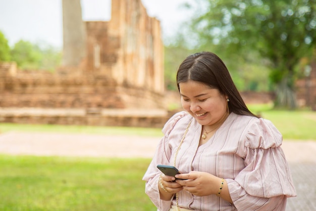 Smiling chubby Asian woman using a cell phone while traveling in a Buddhist temple in Asia