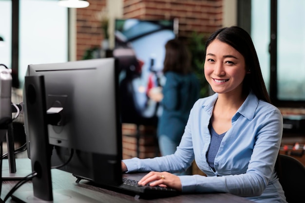 Smiling company employee sitting at desk in office workspace while looking at camera. Creative department team leader developing digital art and professional 3D products.