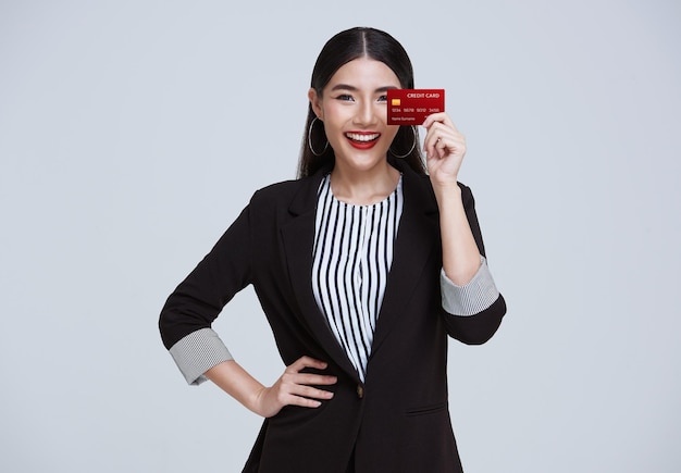 Smiling Confident Asian business woman showing credit card isolated on gray background