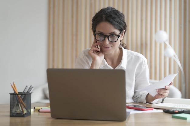 Smiling confident business woman works on computer at home consulting clients distantly online