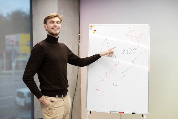 Smiling confident businessman pointing to graph drawn on flipchart Handsome man in modern office