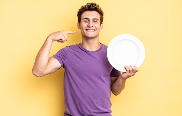 Smiling confidently pointing to own broad smile, positive, relaxed, satisfied attitude. empty plate concept