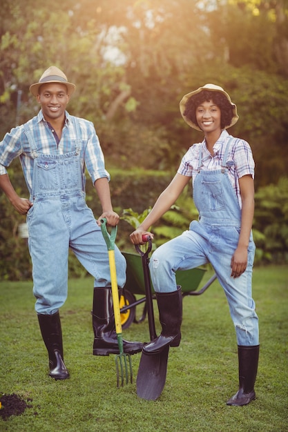 Smiling couple holding shovel and rake in the garden