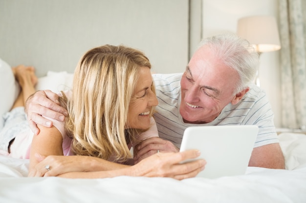 Smiling couple lying on bed and using laptop