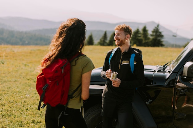 Smiling couple preparing hiking adventure with backpacks by terrain vehicle