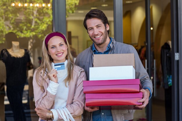 Smiling couple showing credit card and carrying boxes