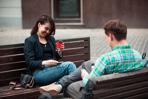 Smiling couple sitting on bench talking to each other drinking coffee