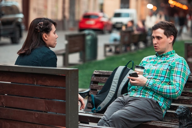 smiling couple sitting on bench talking to each other drinking coffee