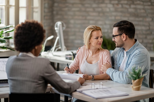 Photo smiling couple talking while woman is signing a contract during the meeting with insurance agent in the office