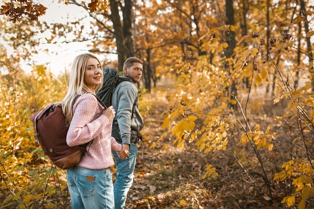 Smiling couple of tourists walking along a forest path holding hands and looking back at camera