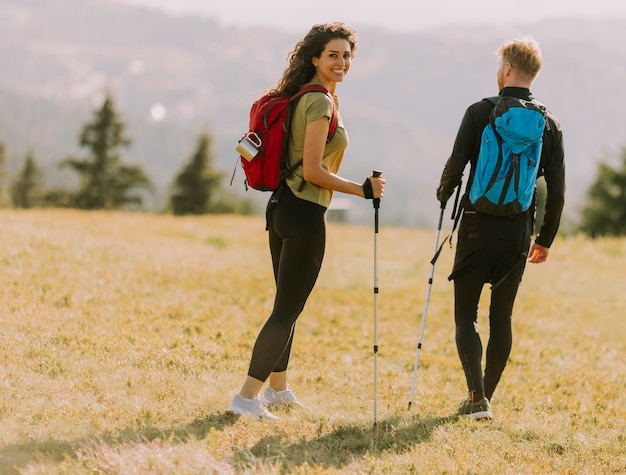 Smiling couple walking with backpacks over green hills