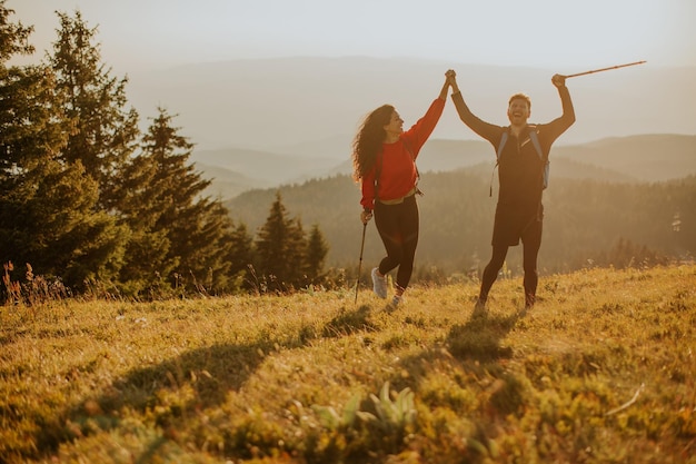 Smiling couple walking with backpacks over green hills