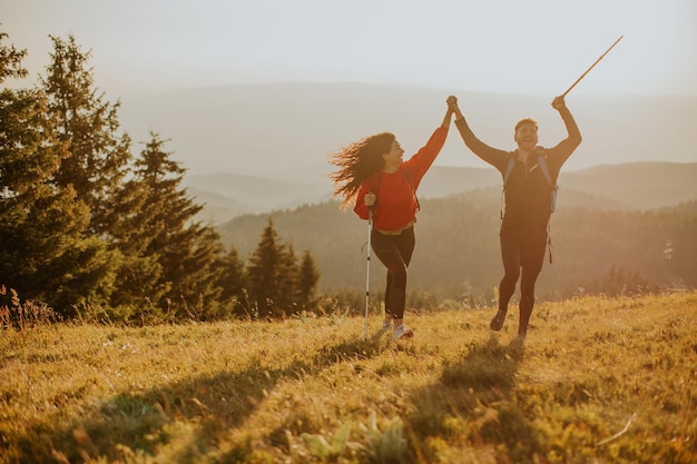 Smiling couple walking with backpacks over green hills