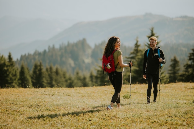 Smiling couple walking with backpacks over green hills