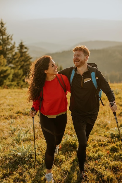 Smiling couple walking with backpacks over green hills