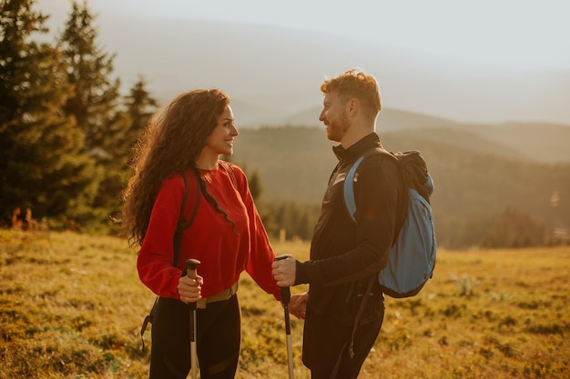 Smiling couple walking with backpacks over green hills