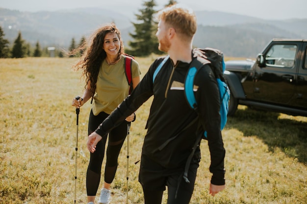 Smiling couple walking with backpacks over green hills