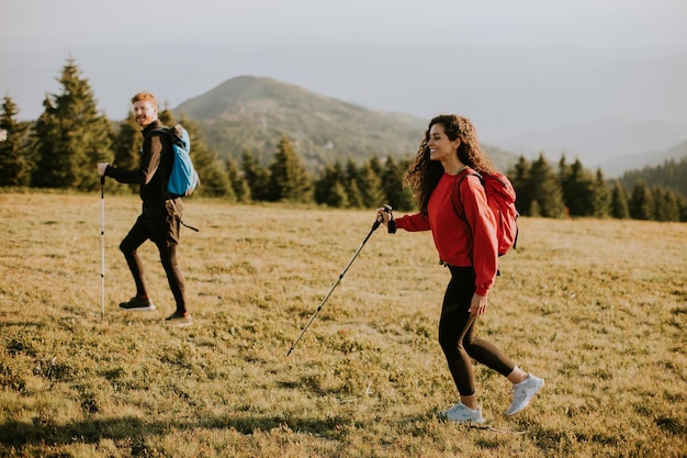 Smiling couple walking with backpacks over green hills