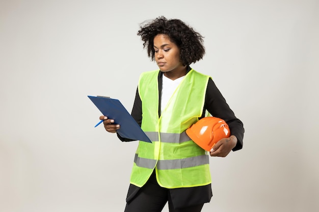 Smiling curly woman with helmet and folder in hands on white background