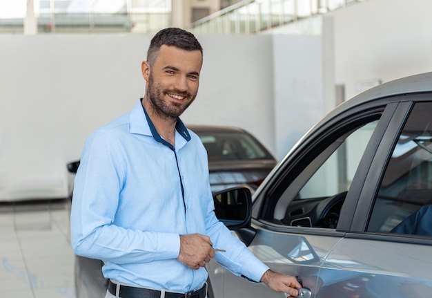 Smiling customer opening the doorknob of his own just bought car at the dealership