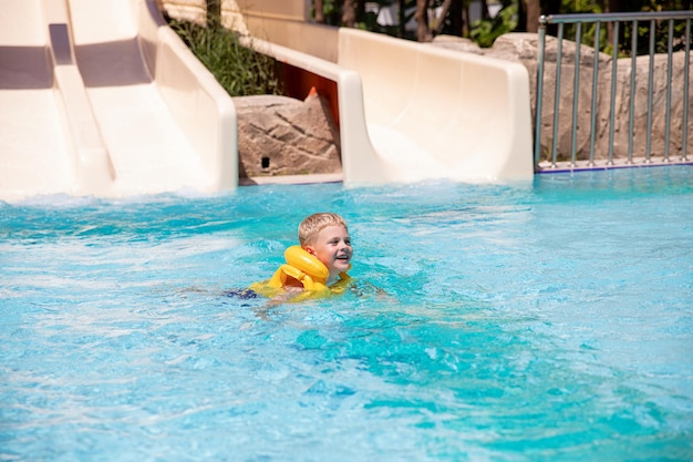 A smiling cute boy in inflatable life jacket has fun in the pool at the aquapark Concept rest fun