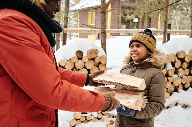 Smiling cute boy with small wooden logs looking at his father while helping him