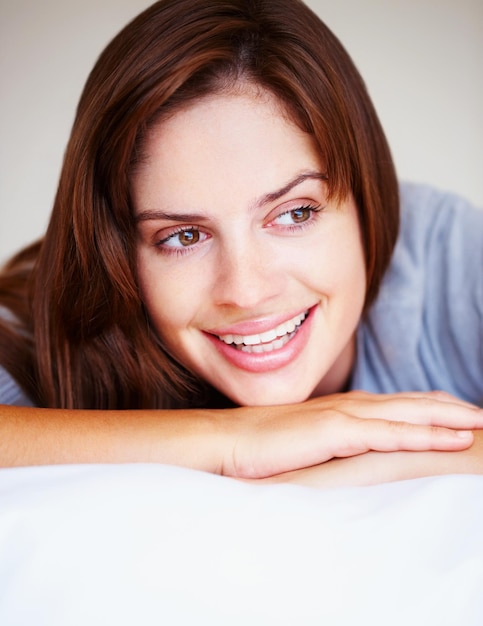 Photo smiling cute female brunette lying on bed closeup portrait of a cute smiling female brunette lying in bed