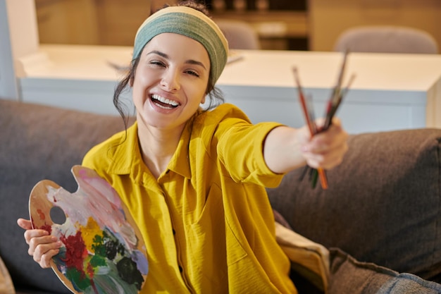 Smiling cute young woman with a palette and brushes in hands