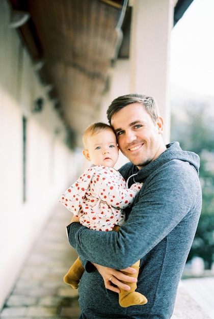 Smiling dad with a baby in his arms stands on the terrace Portrait